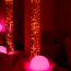 In einem dunklen Raum leuchtet eine grosse Lavalampe und eine runde rosarote Lampe ligt zwischen einem Kissen auf einer Sitzbox.