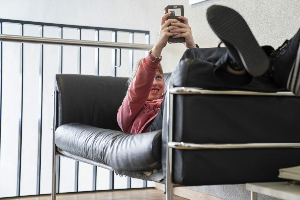 Eine junge Frau surft auf ihrem Handy, während sie auf einem Sofa liegt.