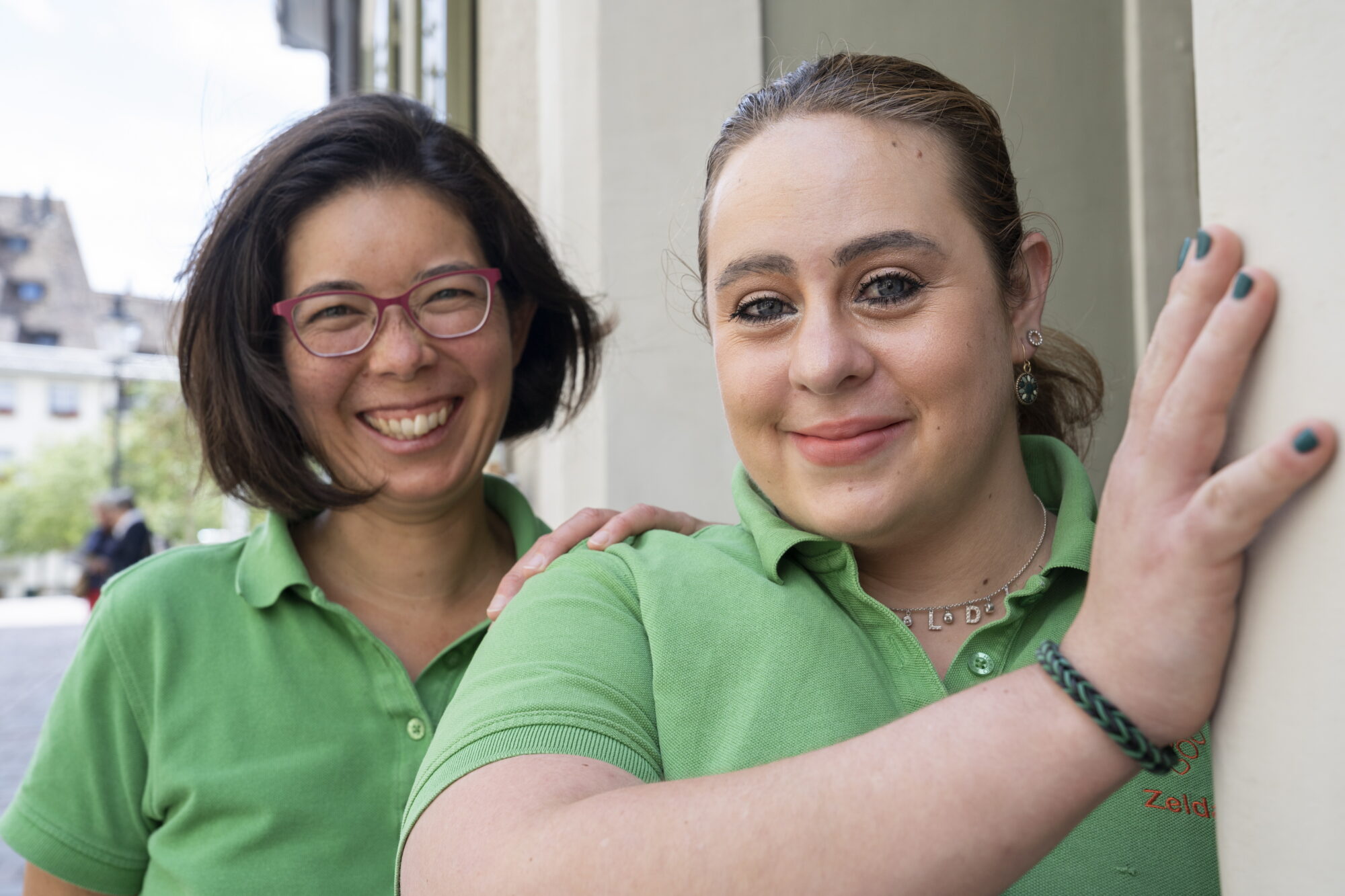 Zwei grün gekleidete Frauen lächeln und starren in die Kamera.