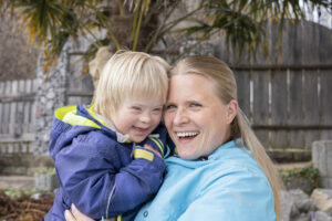 Une maman tient dans ses bras son fils qui vit avec une trisomie 21. Tous deux rient.