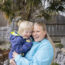 Eine Mutter hält ihren Sohn mit Trisomie21 auf dem Arm und sie lachen beide.