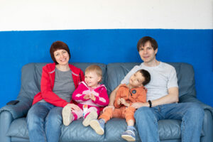 Die Familie sitzt auf einem blauen Sofa im Gemeinschaftsraum des Aufnahmezentrums, in dem sie lebt.