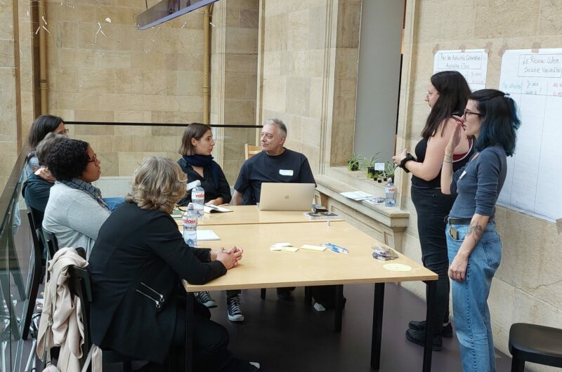 Un groupe de personne échangent autour d'une table avec l'aide d'une interprète en langue des signes.