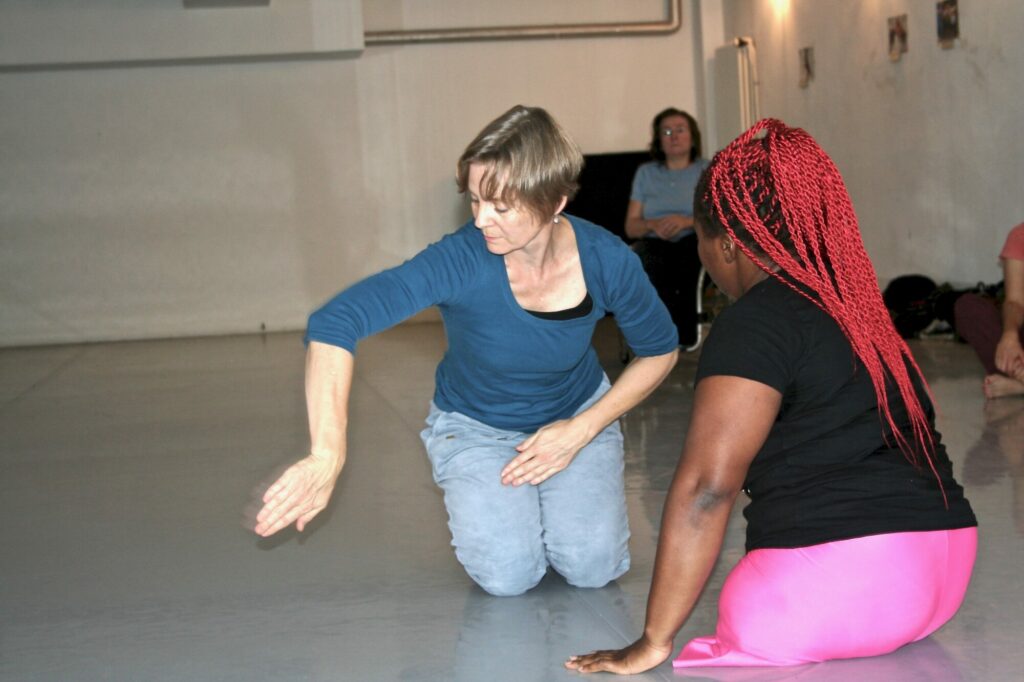 Zwei Frauen sitzen auf dem Boden und tanzen miteinander.