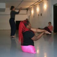Eine Frau ohne Beine mit einer rosafarbenen Leggings liegt am Boden und macht Bewegungen mit ihren Händen.