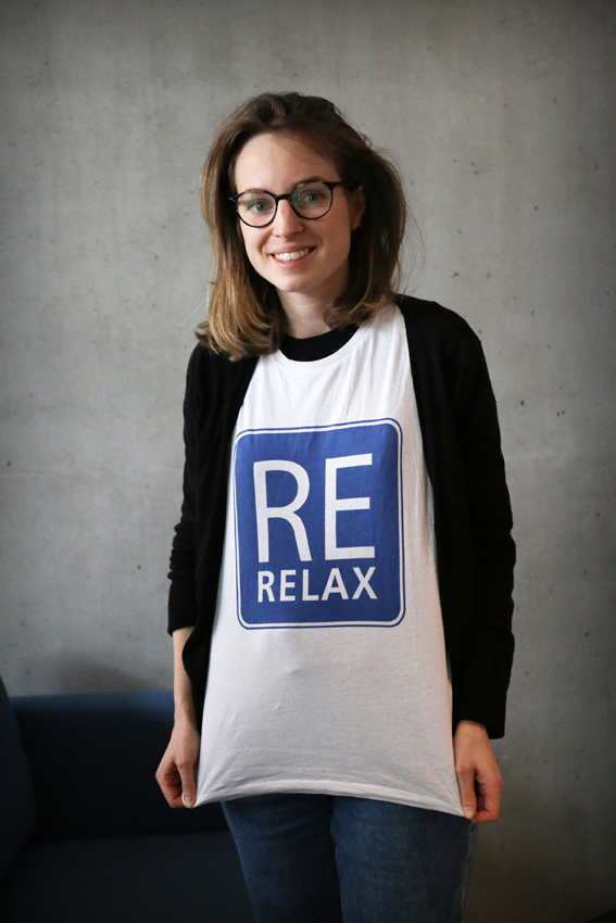 Eine Frau mit einem T-Shirt mit der Aufschrift "RE-Relax" lächelt in die Kamera.