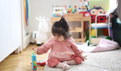 Ein kleines Mädchen sitzt auf dem Boden und spielt.